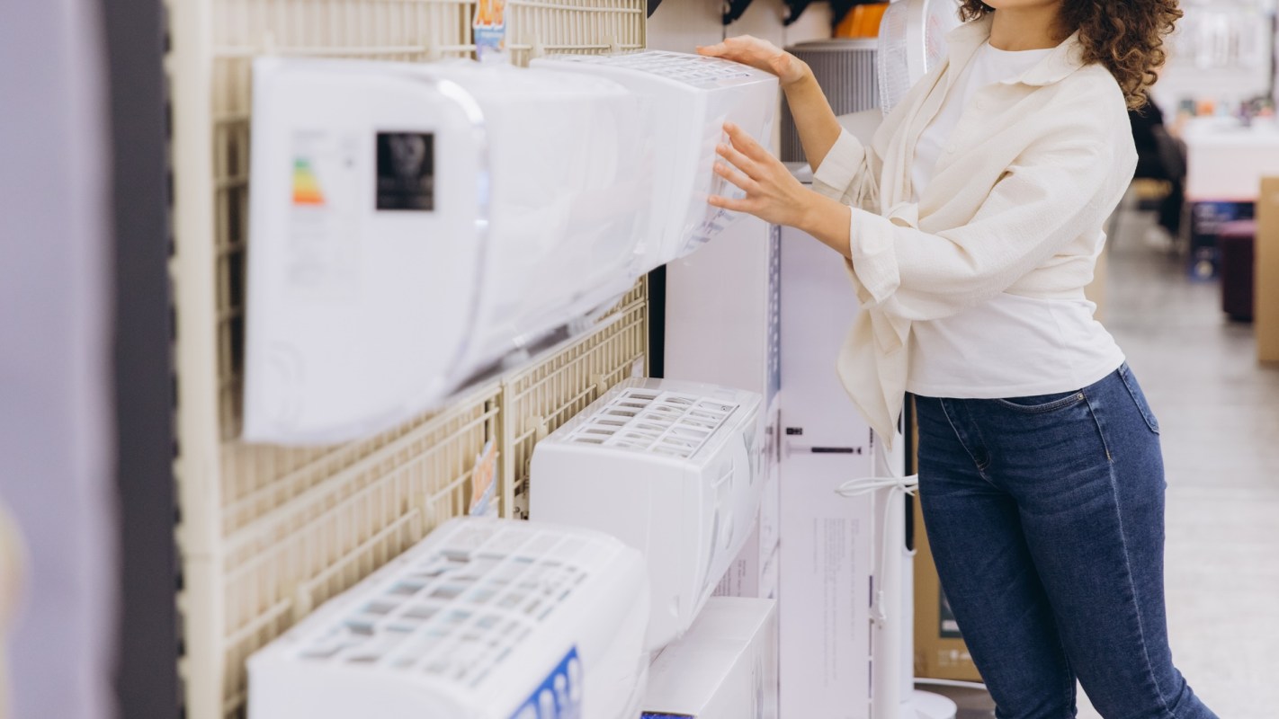 A woman examines air conditioning units on display in a store.
