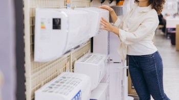 A woman examines air conditioning units on display in a store.