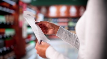 A person holds a grocery receipt in a store aisle.