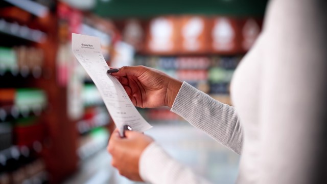 A person holds a grocery receipt in a store aisle.
