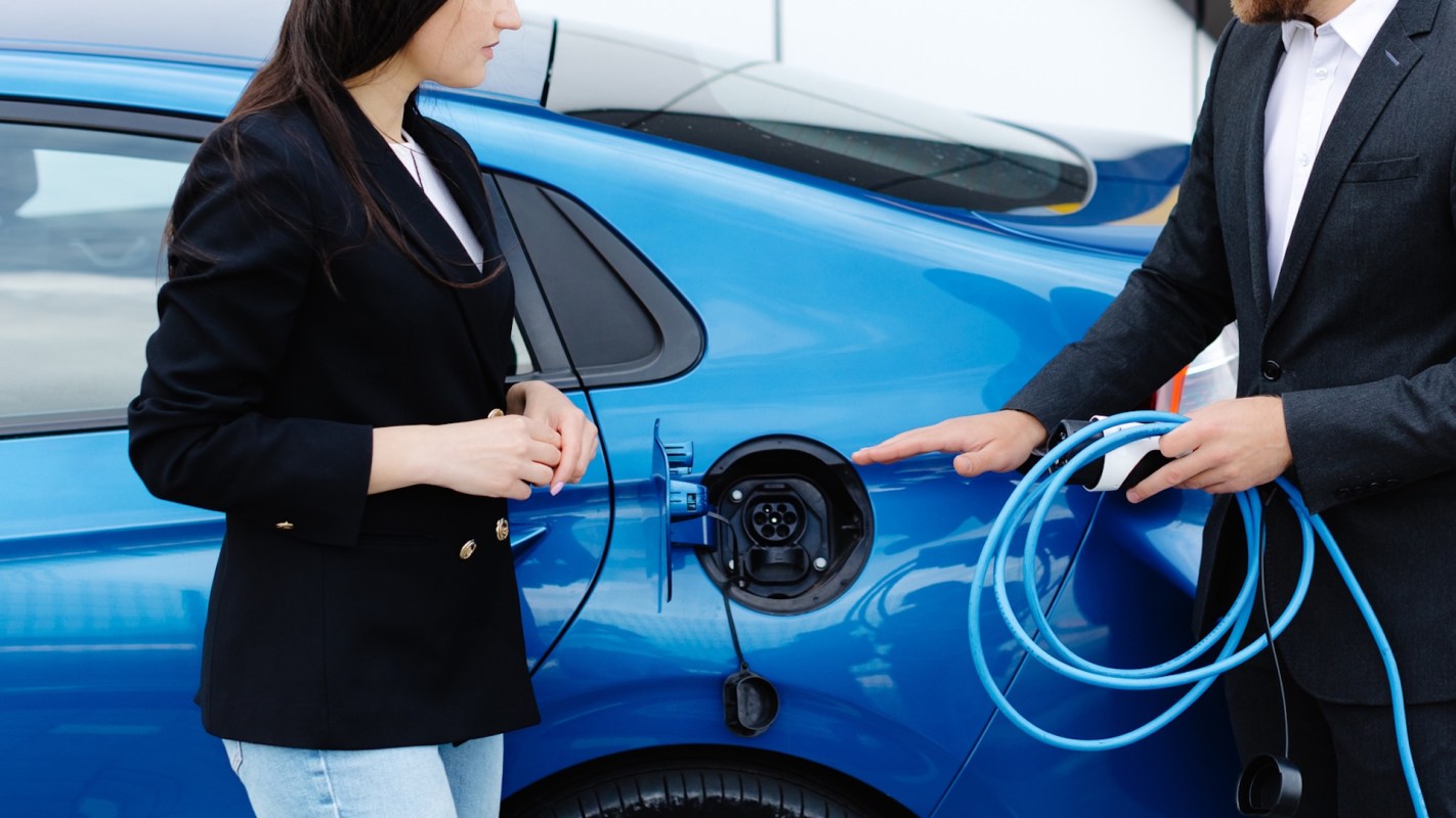 A woman and a man discuss charging an electric vehicle at a charging station.