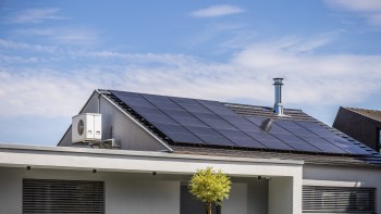 A house with solar panels on the roof and a heat pump unit on the side.