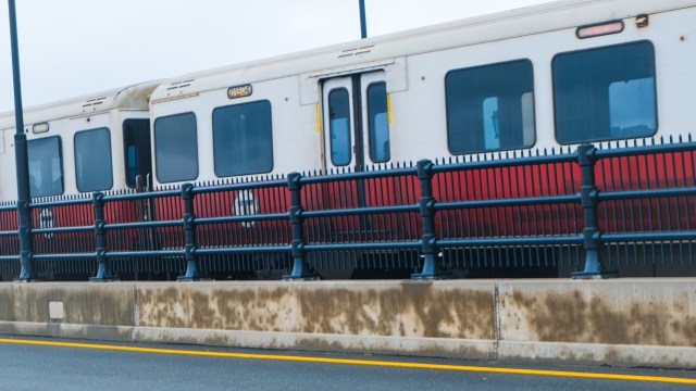 An MBTA train in Boston with its T logo passing along a track with a black railing and concrete barrier on the side.