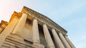 A view of a classical building's columns and detailed architecture against a clear sky.