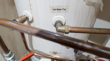 A hot water tap connected to pipes near a water tank.