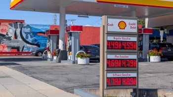 A gas station with a price board displaying gasoline prices and a mural in the background.