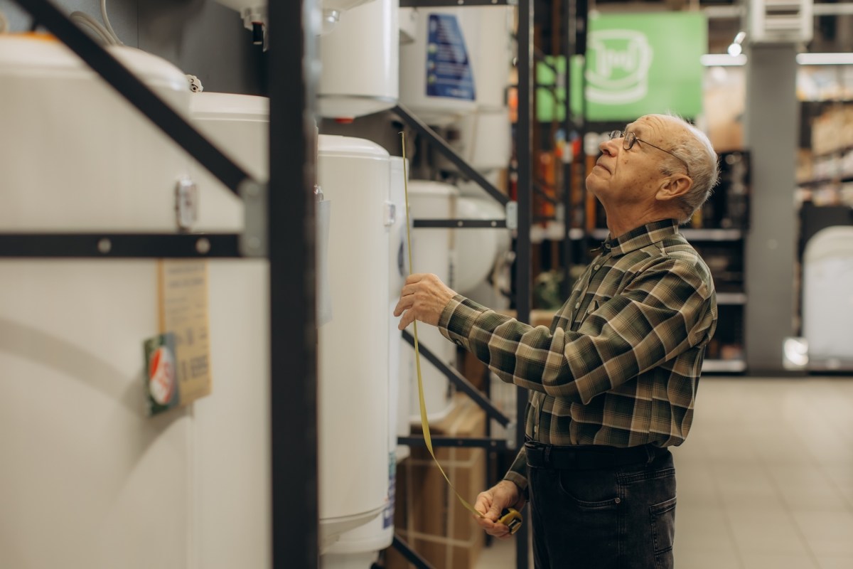 An elderly man measuring the height of a water heater in a home improvement store.