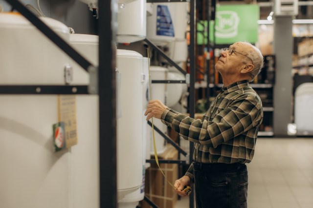 An elderly man measuring the height of a water heater in a home improvement store.