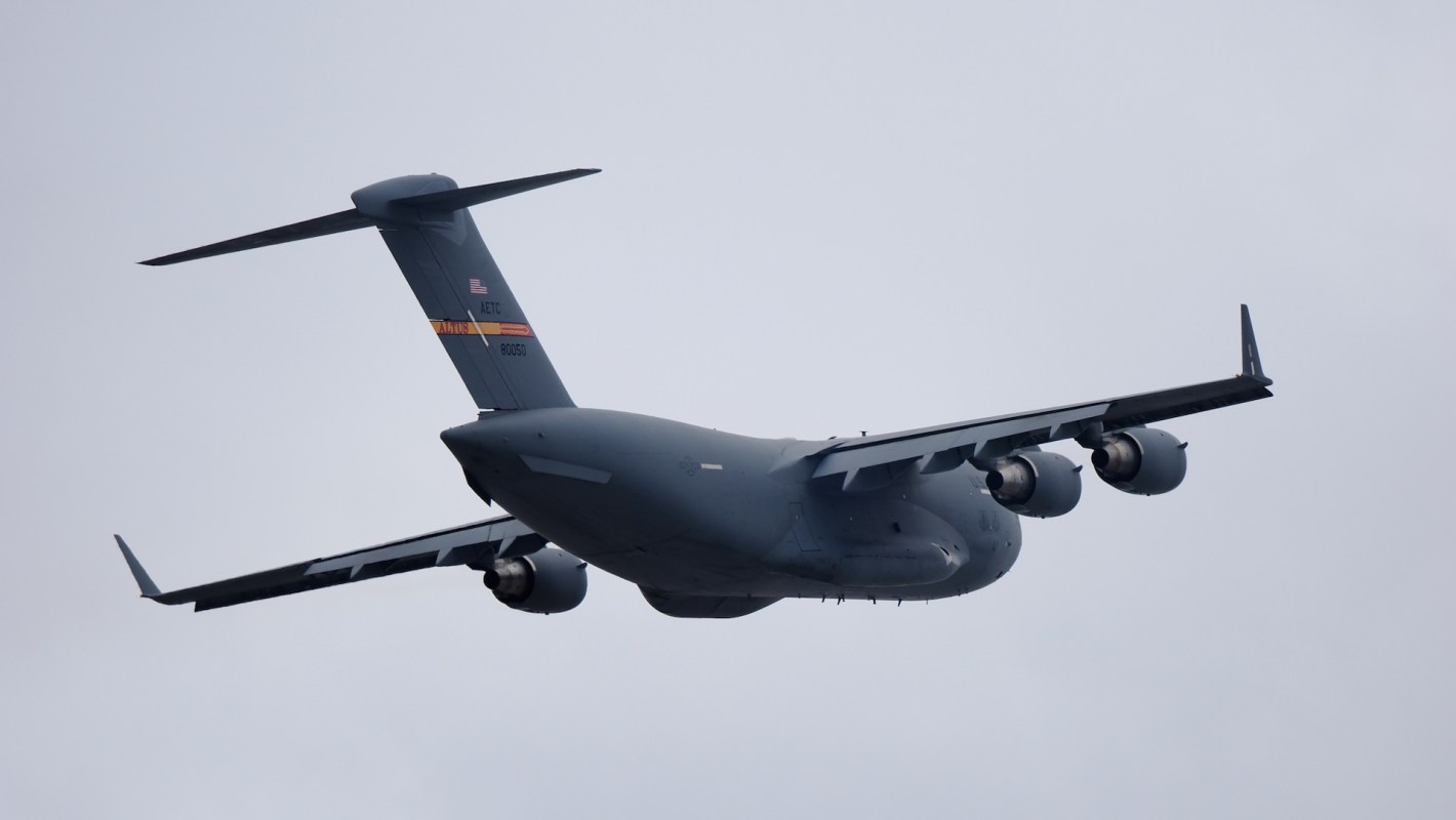 A U.S. military cargo plane flying against a cloudy sky.
