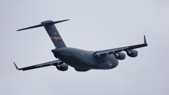 A U.S. military cargo plane flying against a cloudy sky.