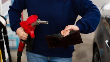 A person holding a fuel nozzle and an empty-looking wallet at a gas station.