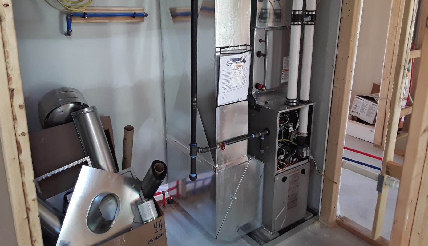 A heating system with pipes and metal ductwork is installed in an unfinished room.