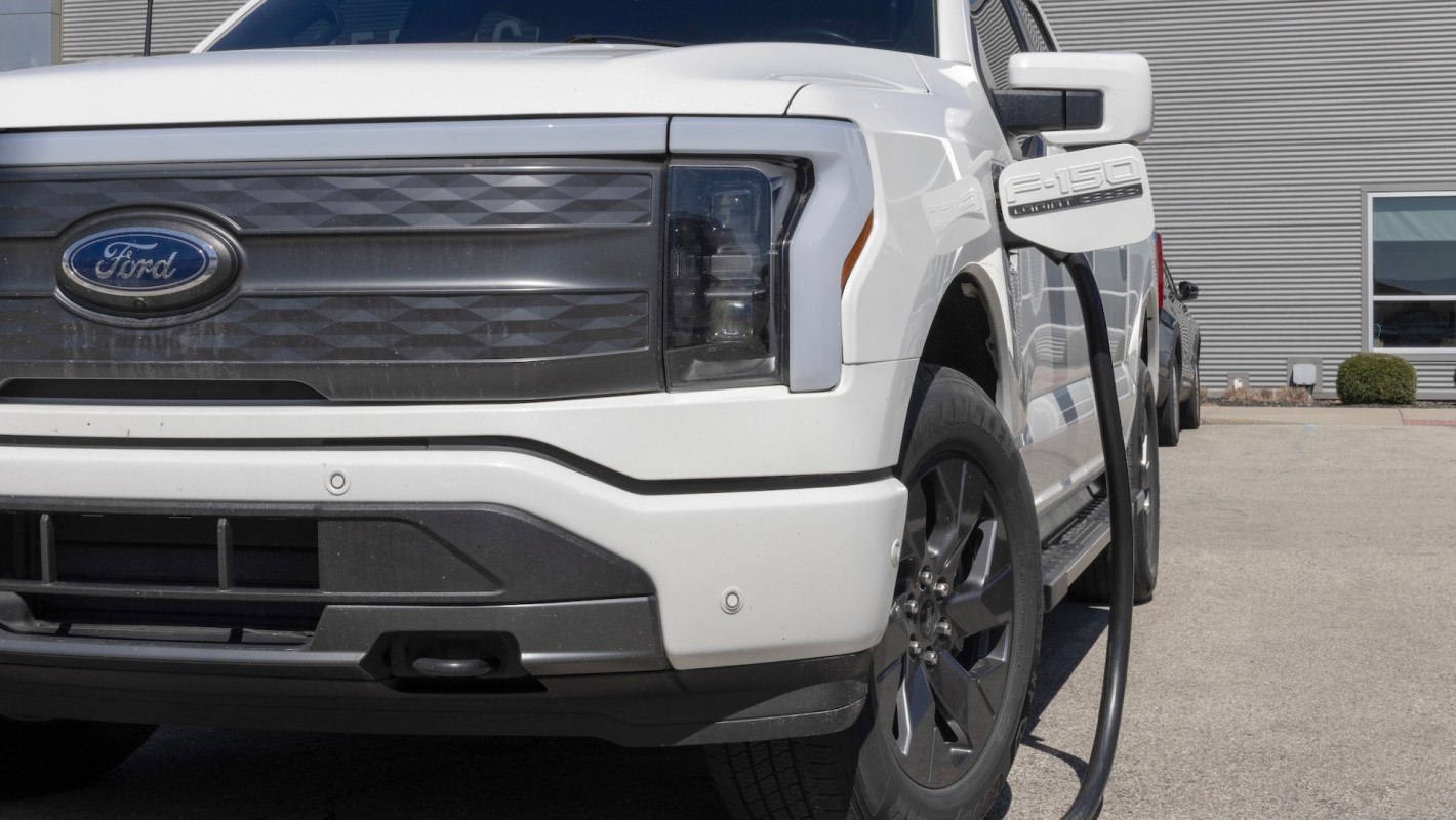 A white Ford F-150 Lightning electric truck charging at a station.