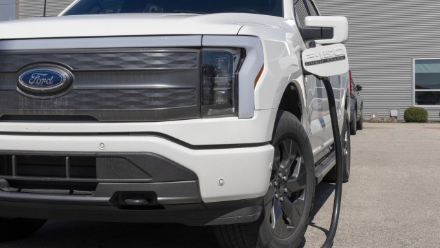 A white Ford F-150 Lightning electric truck charging at a station.
