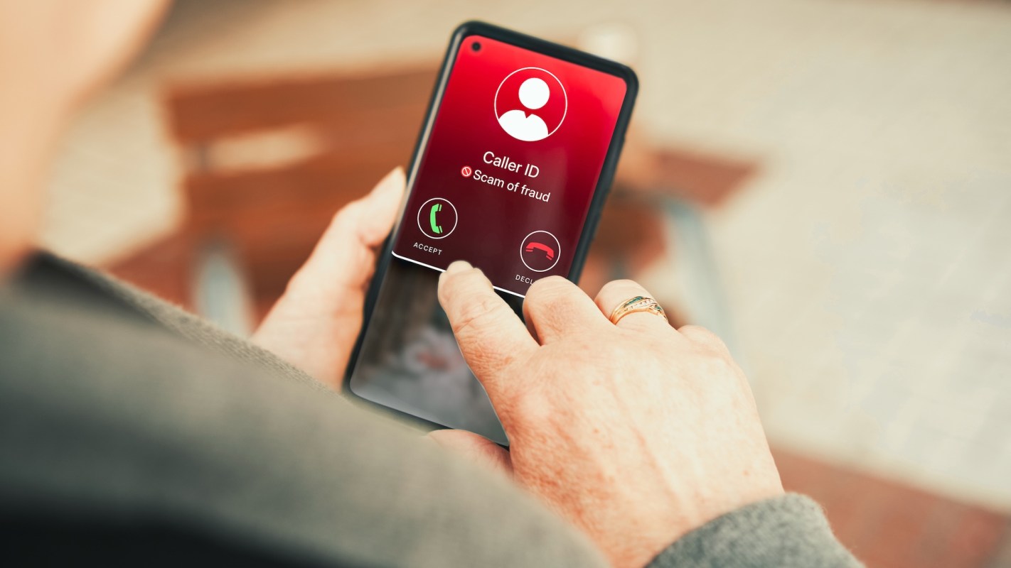 A hand holding a smartphone displaying a caller ID for a suspected scam.