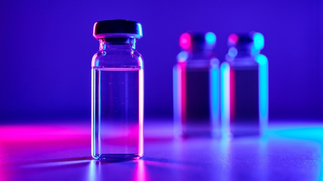 A glass vial with a black cap, illuminated by colorful lights, with blurry vials in the background.