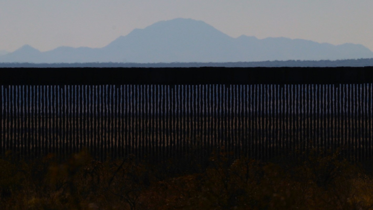 A border wall with mountains in the background under a clear sky.
