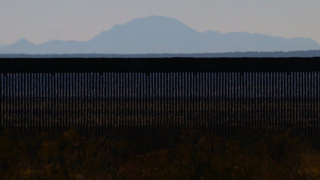 A border wall with mountains in the background under a clear sky.