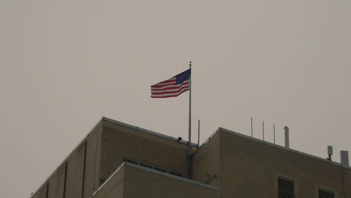 An American flag flies from the rooftop of a building against a gray sky.