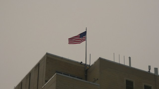 An American flag flies from the rooftop of a building against a gray sky.