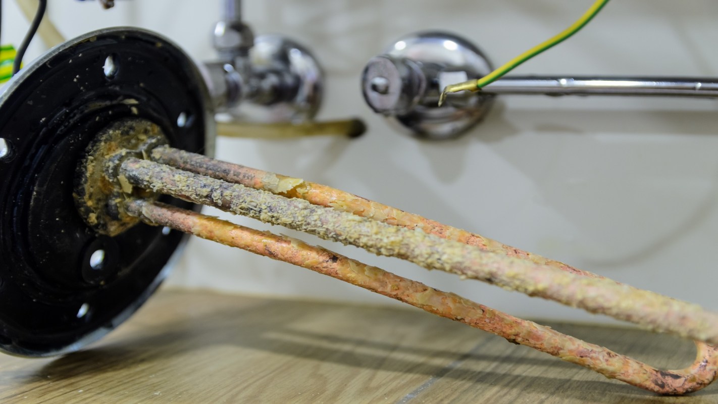A close-up of a corroded heating element attached to a black circular base, positioned near metallic fittings.
