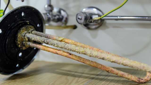 A close-up of a corroded heating element attached to a black circular base, positioned near metallic fittings.