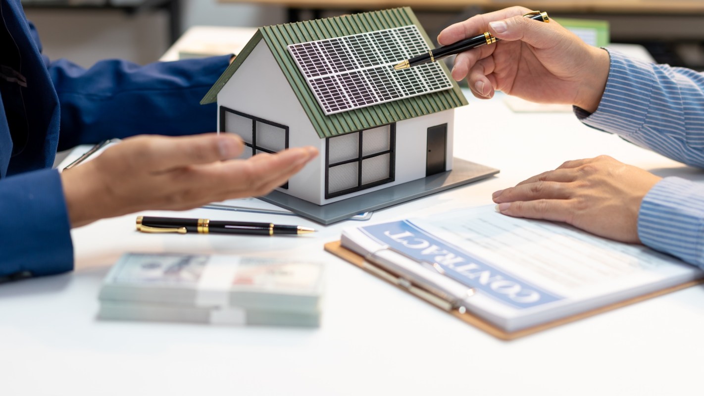 A model house with solar panels on a table during a discussion between two people.