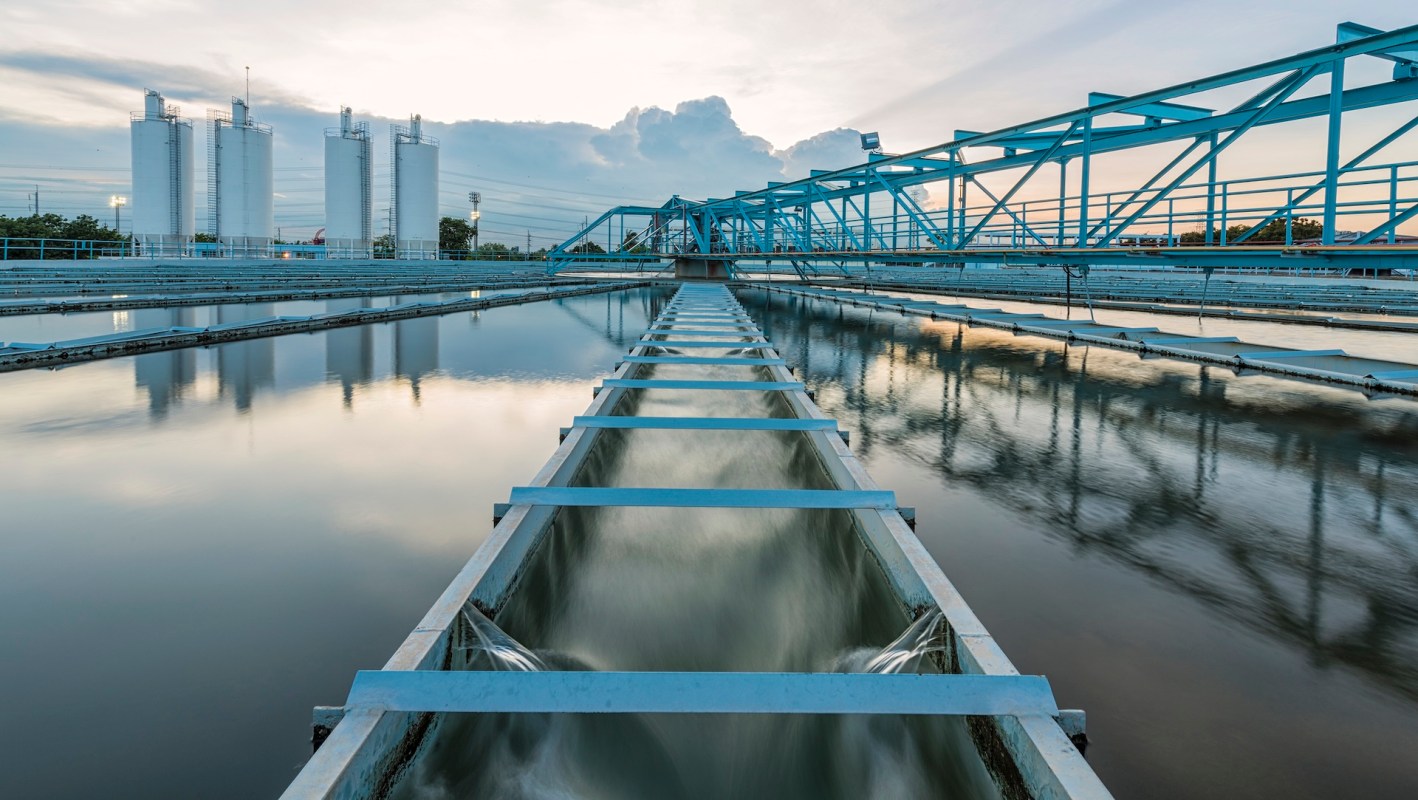 Water treatment facility with infrastructure including channels and storage silos under a cloudy sky.