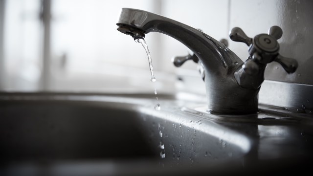 A faucet with water dripping into a metal sink in a dark environment.