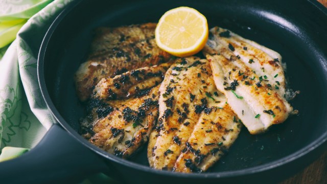 Cooked flounder fillets garnished with herbs and a lemon slice in a frying pan.