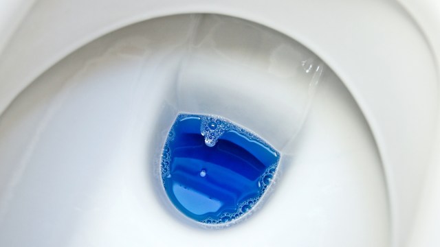 A toilet bowl with blue liquid and bubbles.