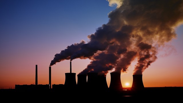 A power plant with cooling towers emitting smoke against a sunset sky.