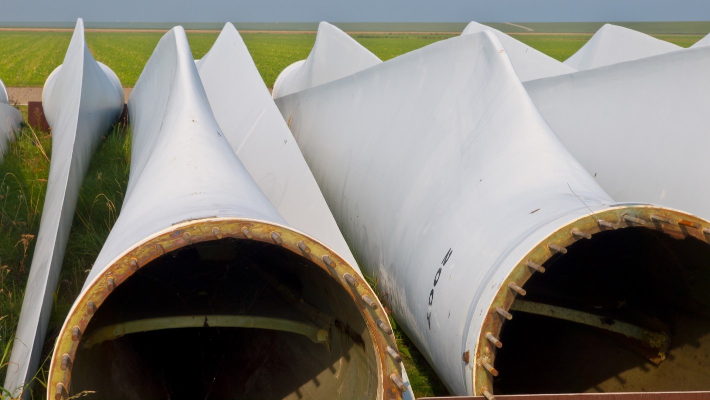 Several large wind turbine blades are laid on the ground, surrounded by grass and open fields.