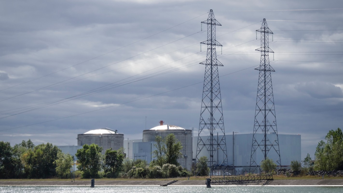 A nuclear power plant with cooling towers and high-voltage transmission lines under a cloudy sky.