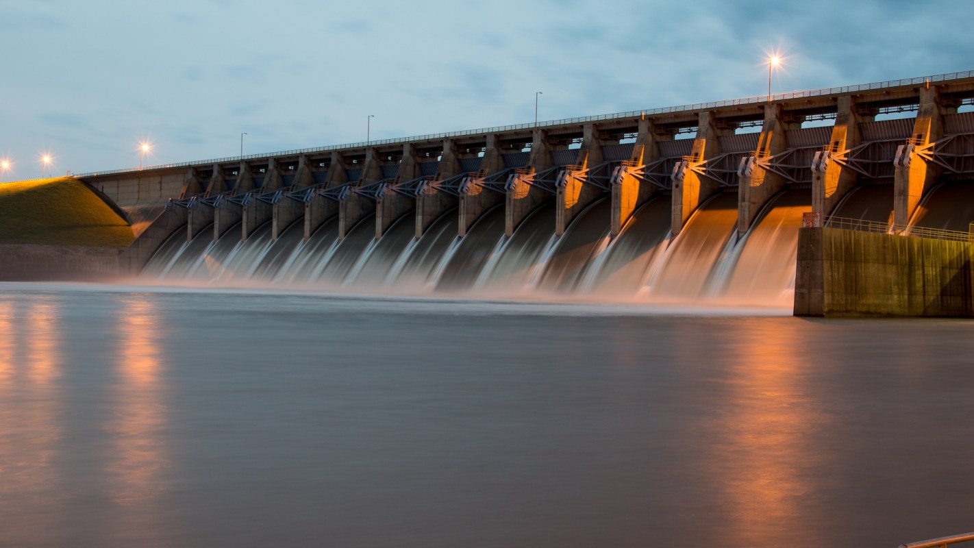 A dam with water flowing over multiple spillways at dusk.