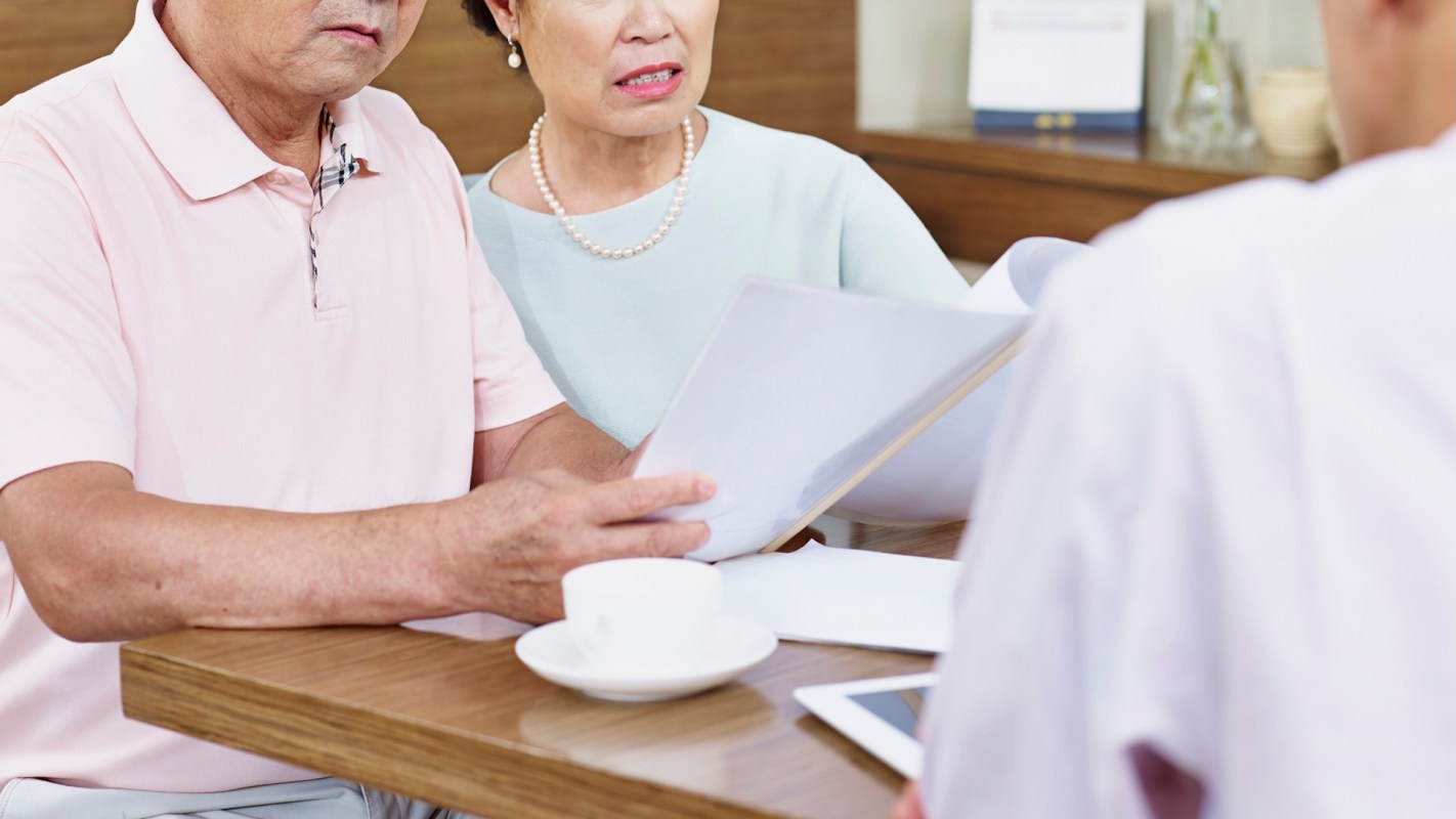 An elderly couple reviews documents at a table.