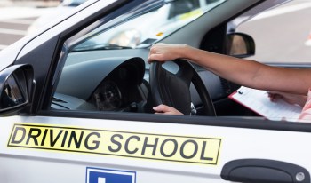 A person driving a car with a "Driving School" sign on the door.