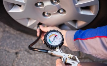 A person uses a pressure gauge to check the air pressure of a car tire.