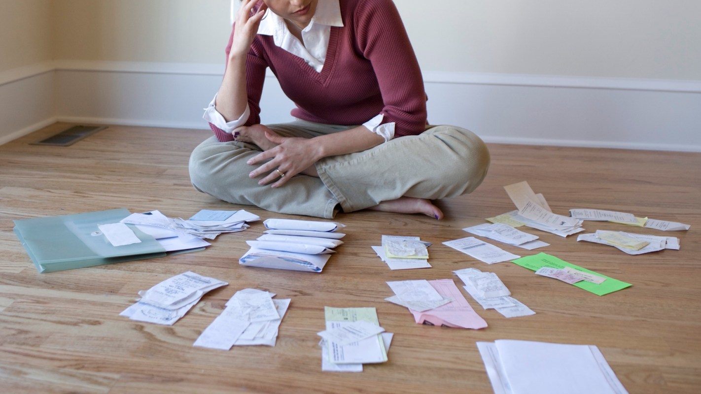 A person sits on the floor surrounded by disorganized receipts and documents.