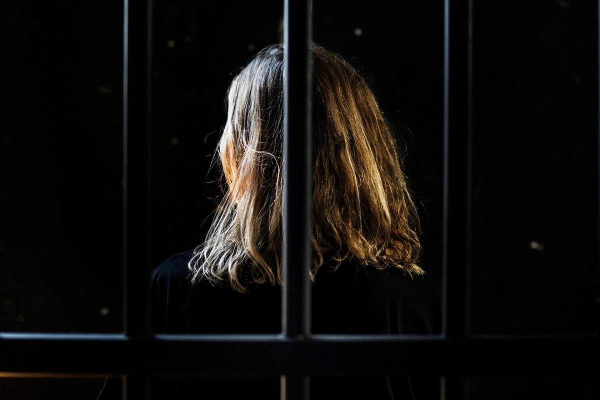 A woman standing behind prison bars with her back to the camera.
