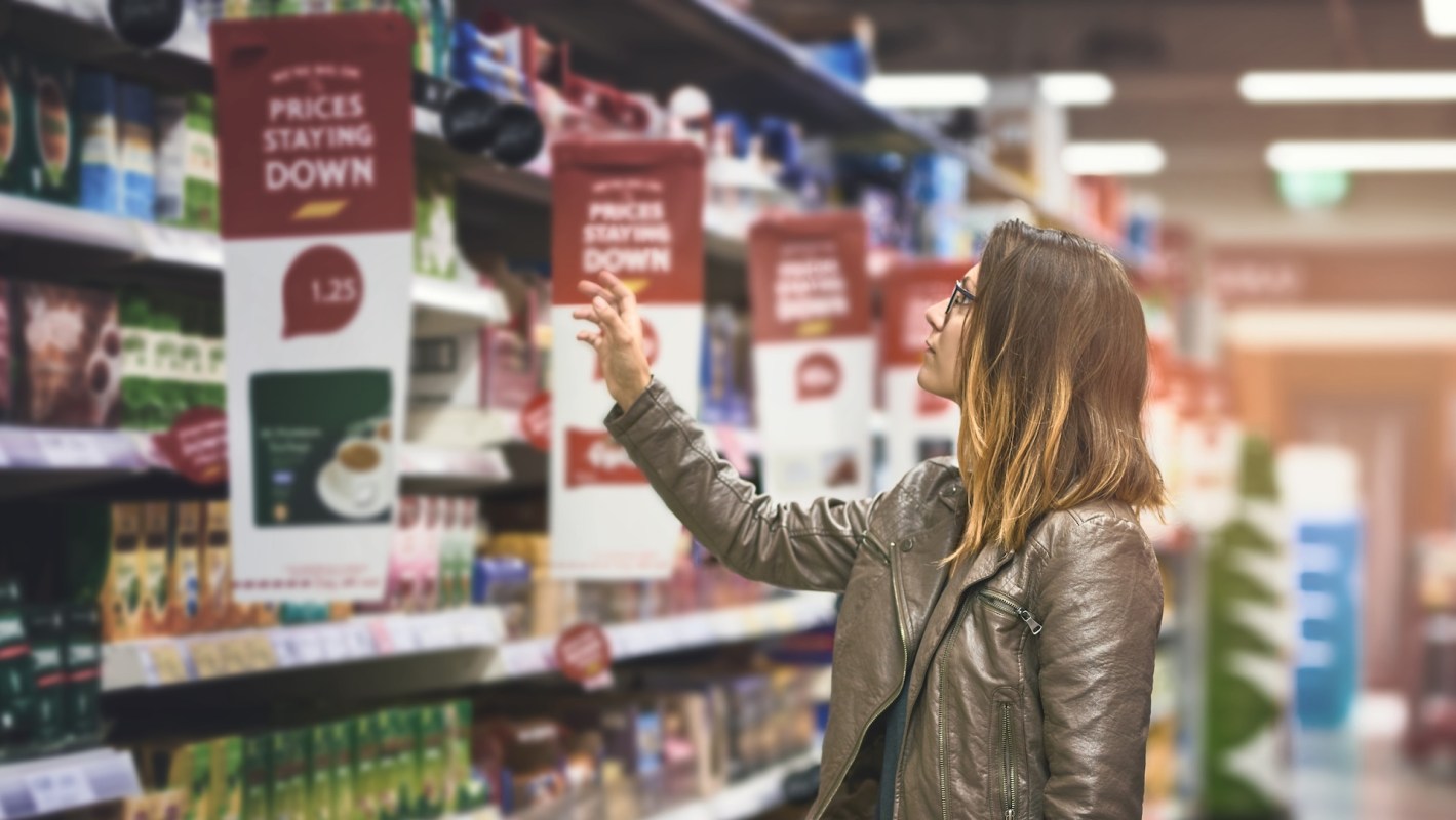 A woman reaches for a product on a grocery store shelf with promotional signs.