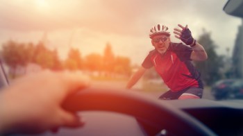 A cyclist waves in anger from the road in front of a car.
