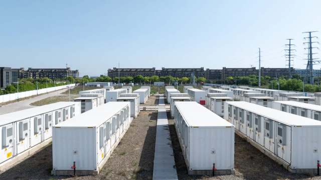 A row of white shipping containers in a semi-industrial area with buildings and greenery in the background.