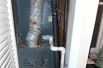 A heating unit with metallic ducts and pipes inside a narrow space.