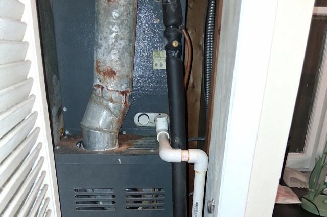 A heating unit with metallic ducts and pipes inside a narrow space.