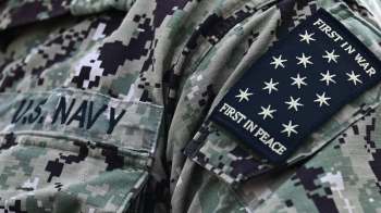 A close-up of a U.S. Navy uniform displaying the insignia "FIRST IN WAR, FIRST IN PEACE."