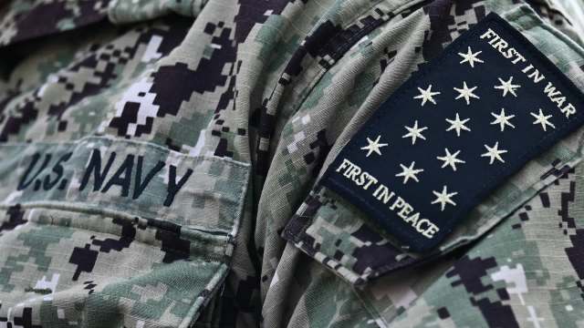 A close-up of a U.S. Navy uniform displaying the insignia "FIRST IN WAR, FIRST IN PEACE."