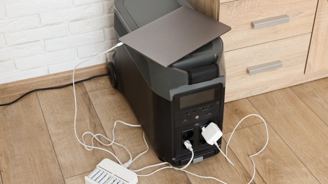 A power station with a laptop and charging cables on a wooden floor near a cabinet.