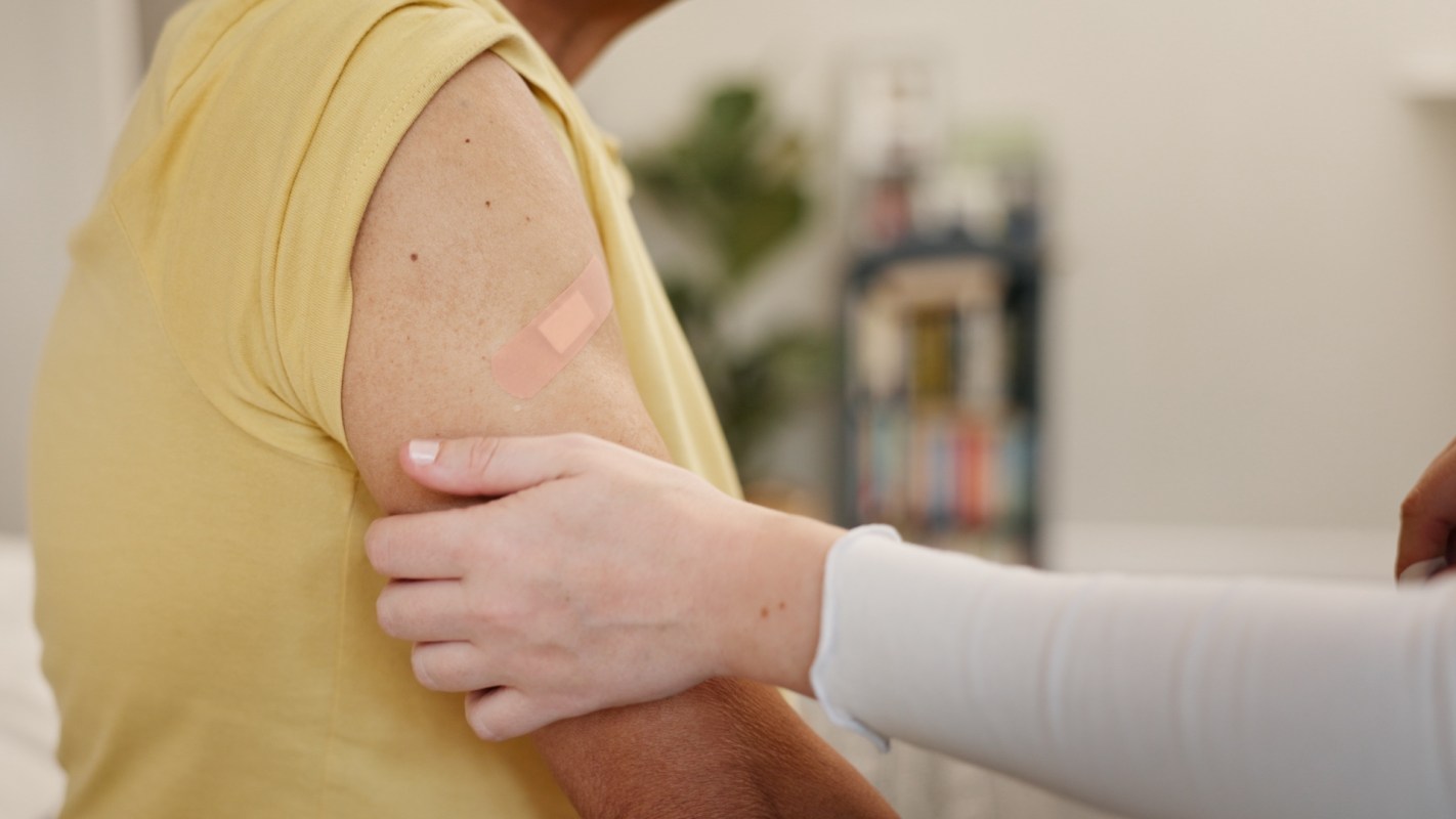 A medical professional gently touches a patient with a bandage on their arm.