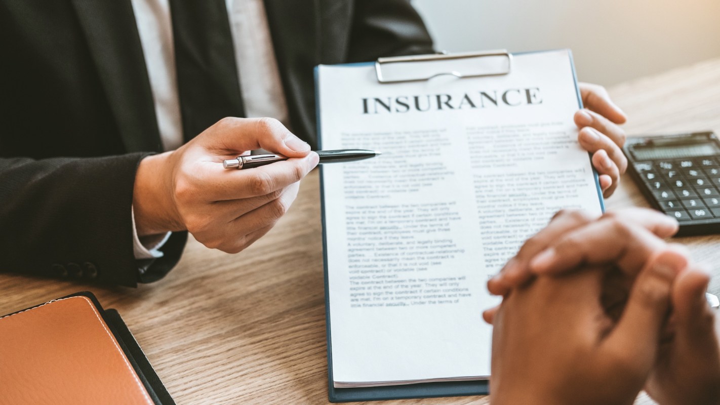 A person points at an insurance document during a discussion at a table with a calculator nearby.